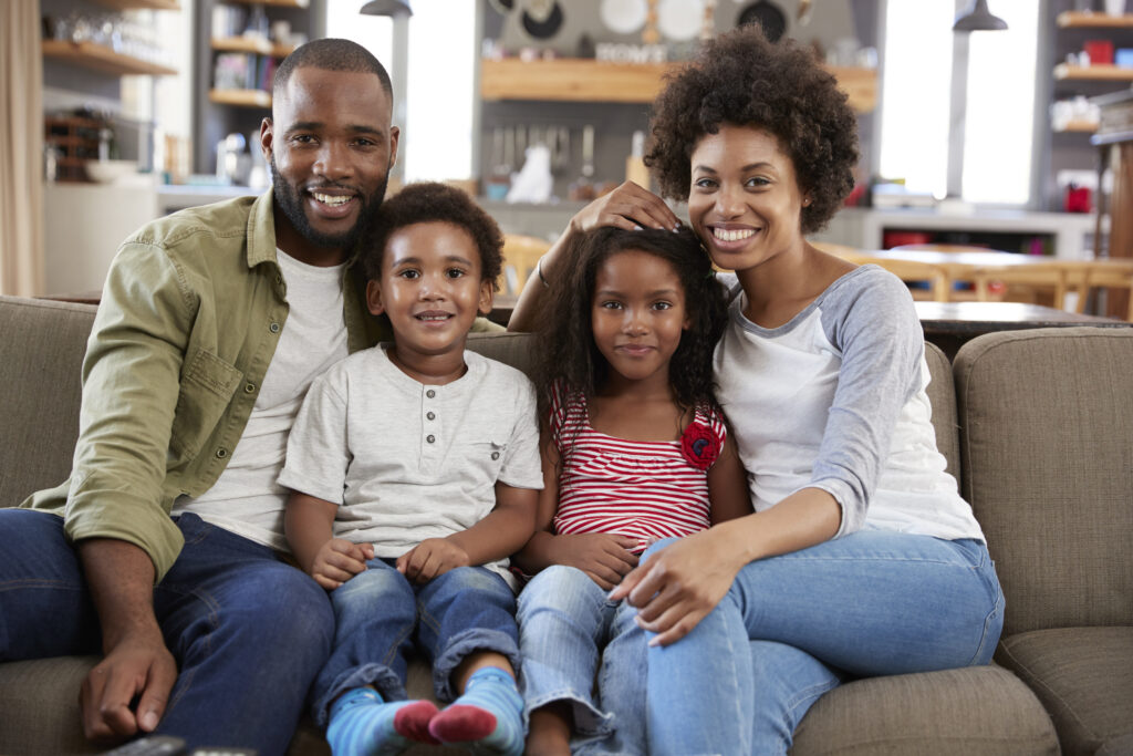 Portrait Of Happy Family Sitting On Sofa In Open Plan Lounge