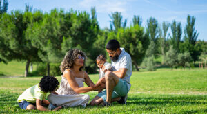 Latino family of father mother son and baby enjoying a sunny day in a park sitting on the grass