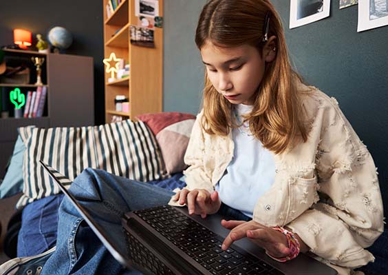 Teen girl does homework on her laptop while sitting in her bedroom