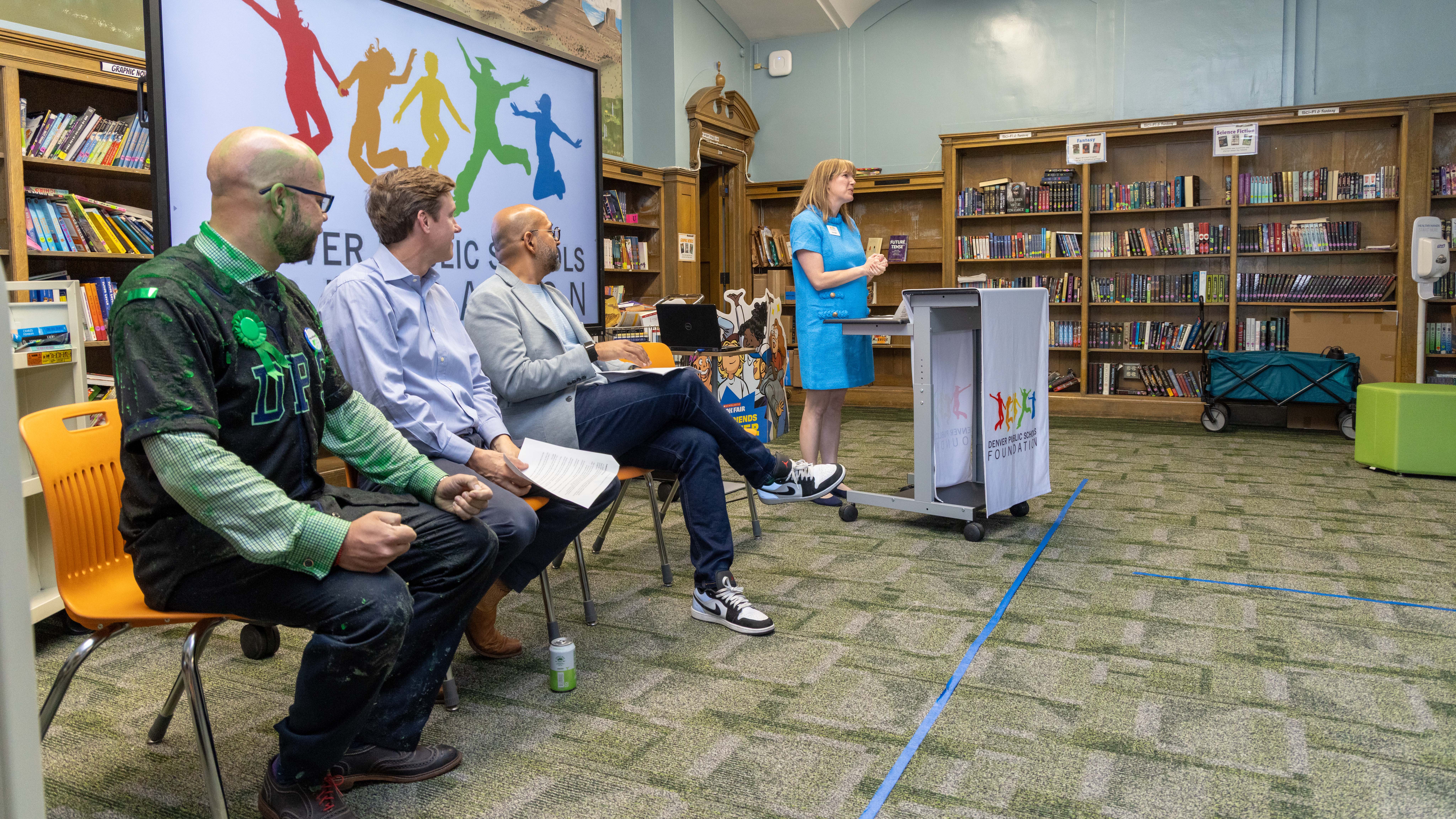 A woman speaks at a podium as three men listen