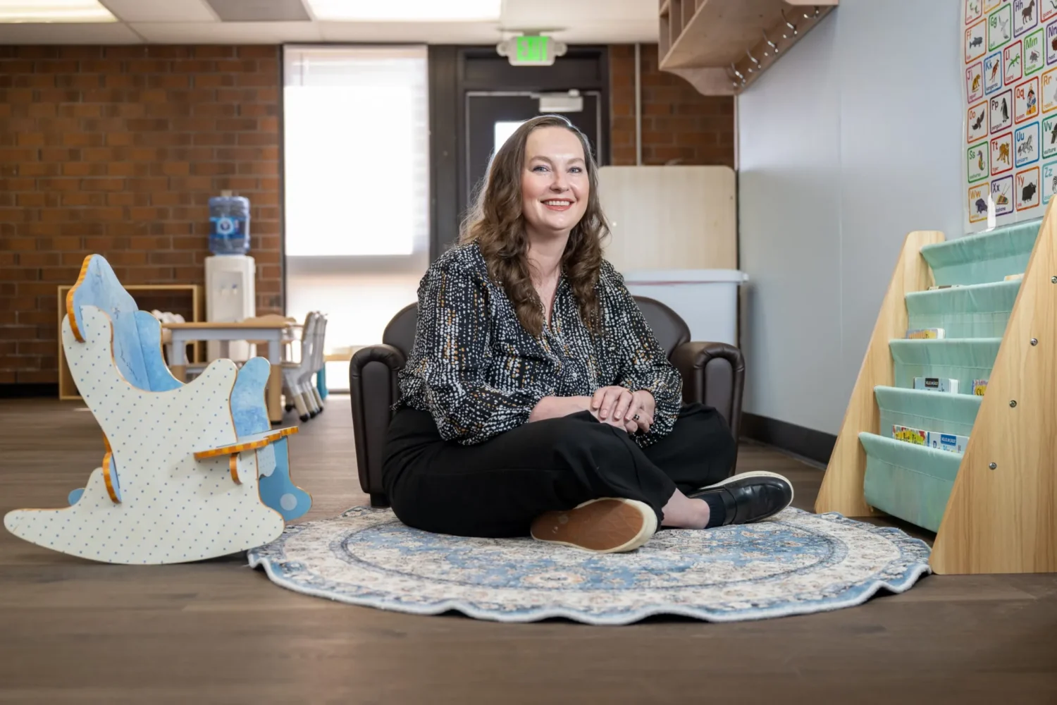 A child care provider sitting on the floor in a classroom