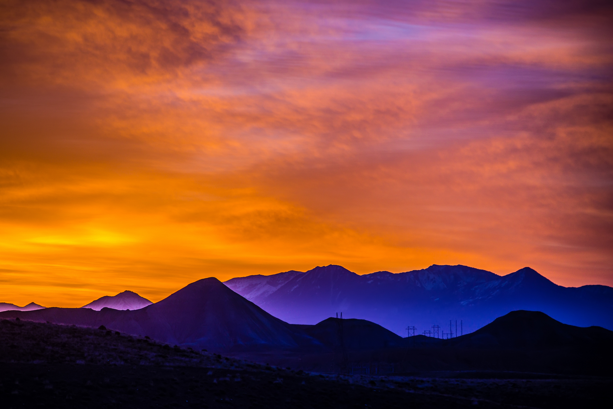 Silhouetted mountains under a vivid sunrise sky filled with deep oranges, purples, and blues.